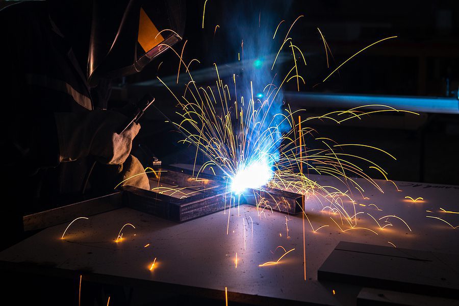 Welding and fabrication specialist with welding sparks flying in a dark room.
