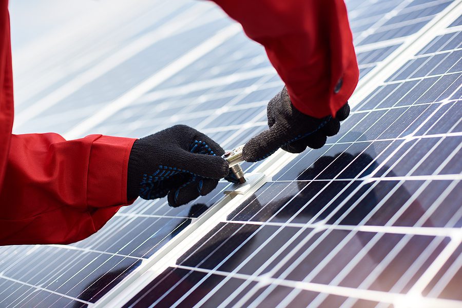 Close-up of hands installing a large solar panel.