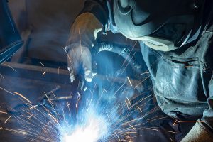 Welding worker wearing industrial uniform and safety gear, welding steel as sparks fly. 