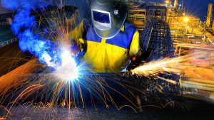 Steel worker wearing safety gear, cutting and welding metal with many sharp colorful sparks flying. 