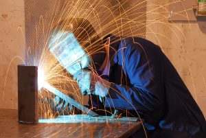 Close up of a welder wearing protective gear welding with sparks flying. 