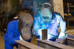 Two welders wearing protective gear work together during a training  session. 