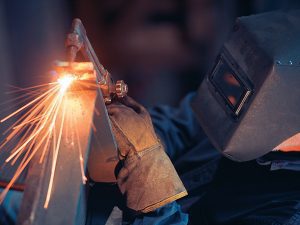 Welder using a tool to cut through a piece of metal with sparks flying. 