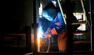 Welder wearing protective gear, working on a project in the dark with sparks. 