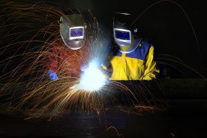 Two welders cutting and welding metal, wearing protective gear with sparks flying. 