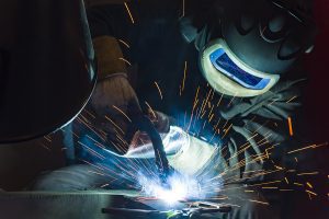 Industrial steel welder wearing protective gear and welding with sparks flying. 