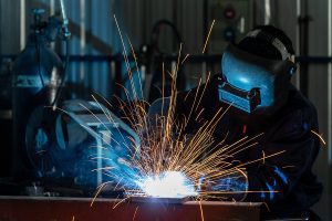 Professional welder working on a metal project in a factory with sparks spreading. 