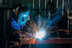 Professional welder wearing protective gear and welding metal with sparks flying. 