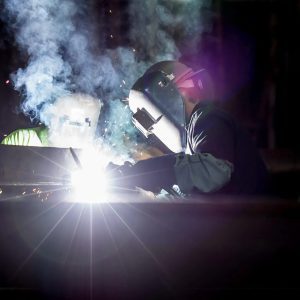 Welder working on a project with sparks flying against a dark background. 